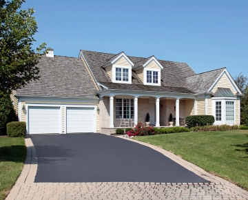 pale yellow house with blacktop and brick driveway
