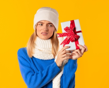 woman holding gift against yellow background with confused look