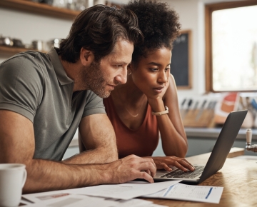 couple looking at laptop on kitchen counter with coffee