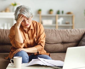 elderly woman in orange shirt distressed sitting on couch with laptop nearby