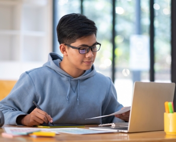 student with glasses looking at laptop and taking notes