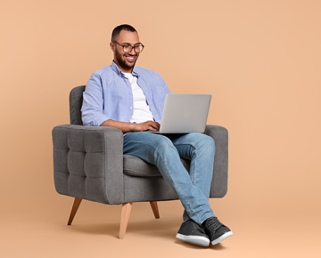 man sitting on gray chair with laptop against orange background
